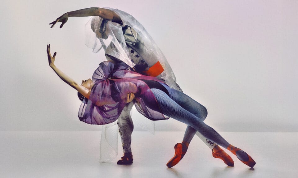 Two dancers strike a pose in an empty room, arms reaching towards each other in an arc.