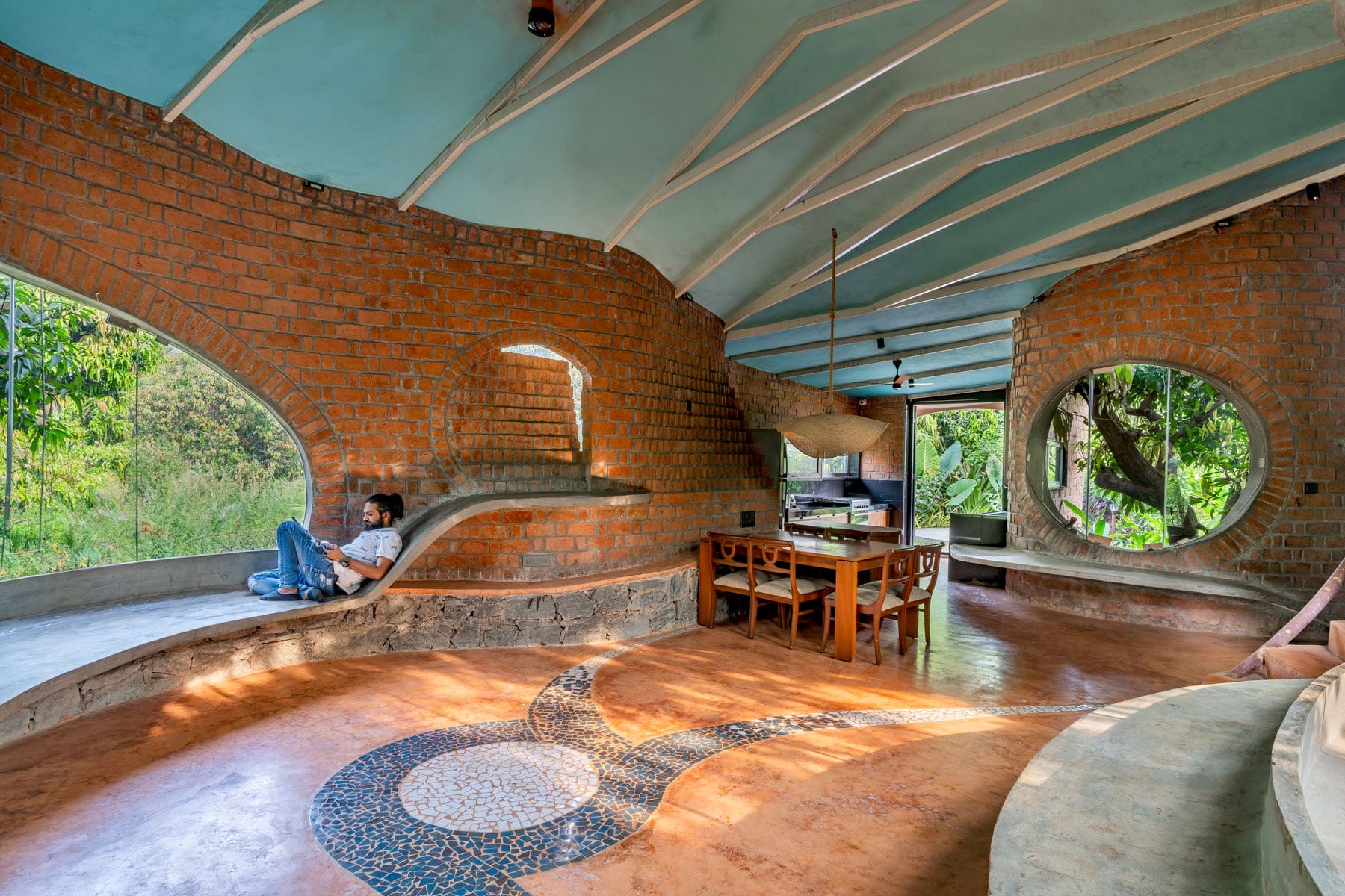 a man sits on a concrete bench in a home with brick walls and large round windows