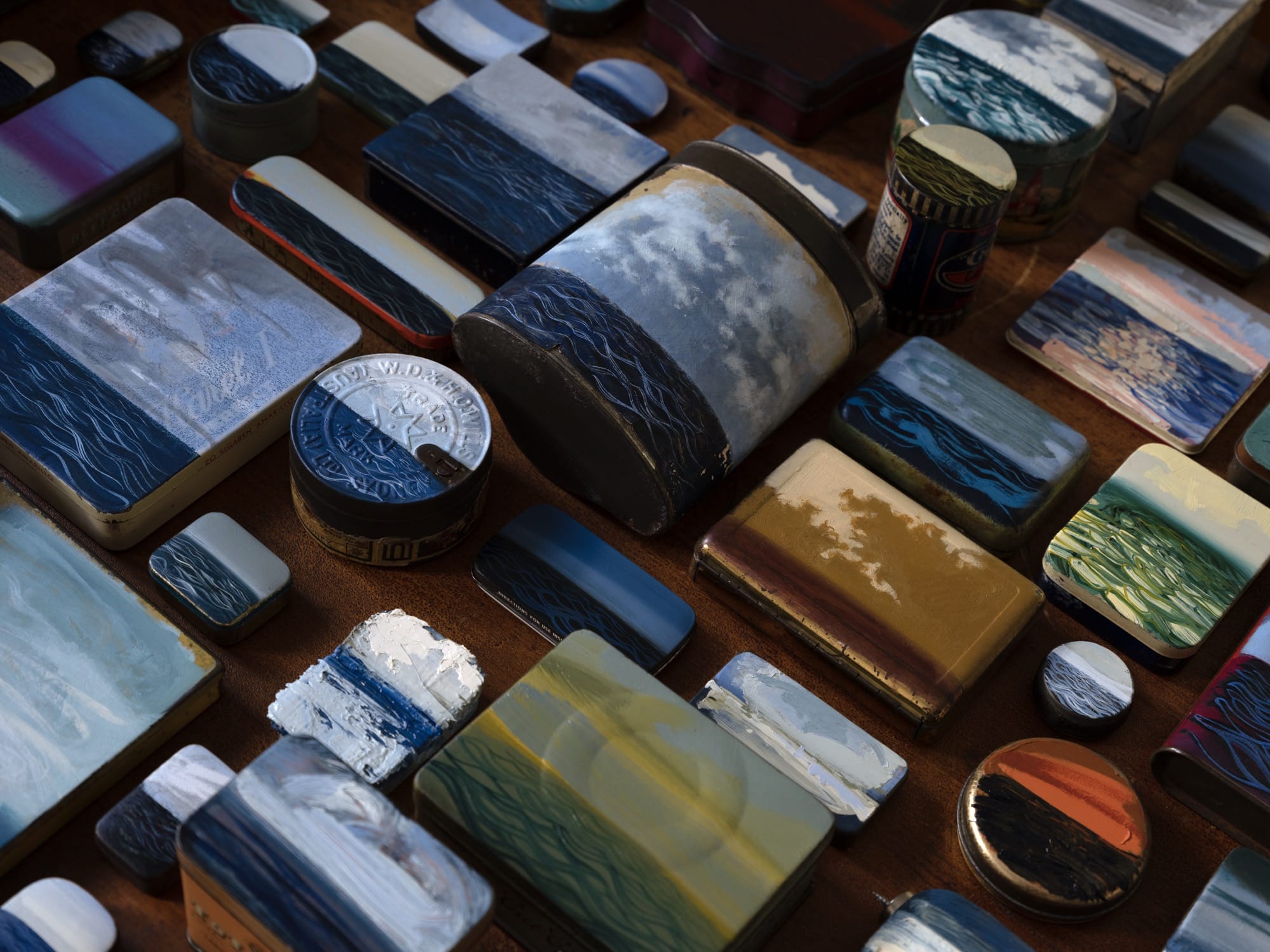 an array of small tins and boxes with paintings of the sea on them, arranged neatly on a table