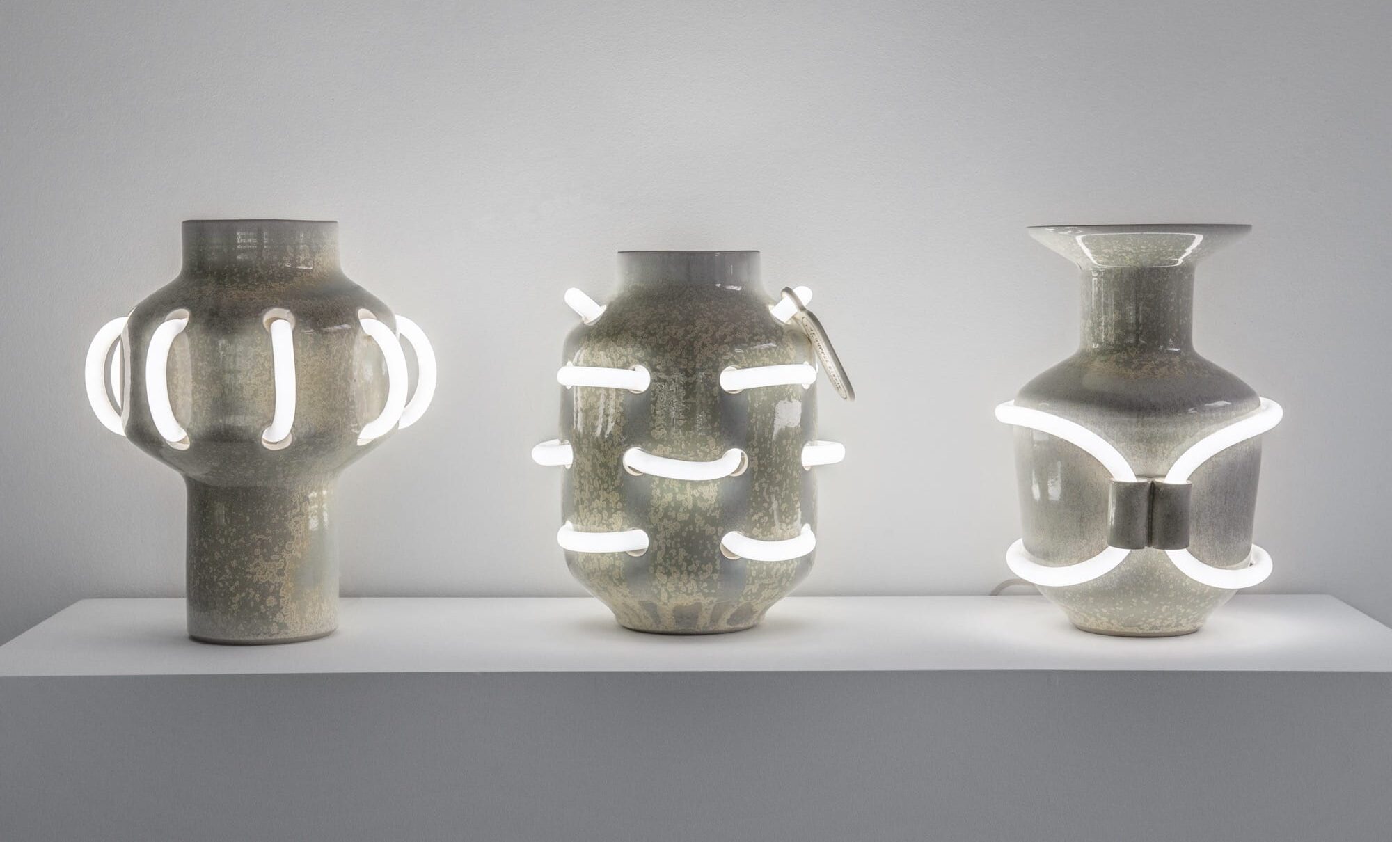 three ceramic vessels with shiny enamel coating that is intersected with curves of white neon lights