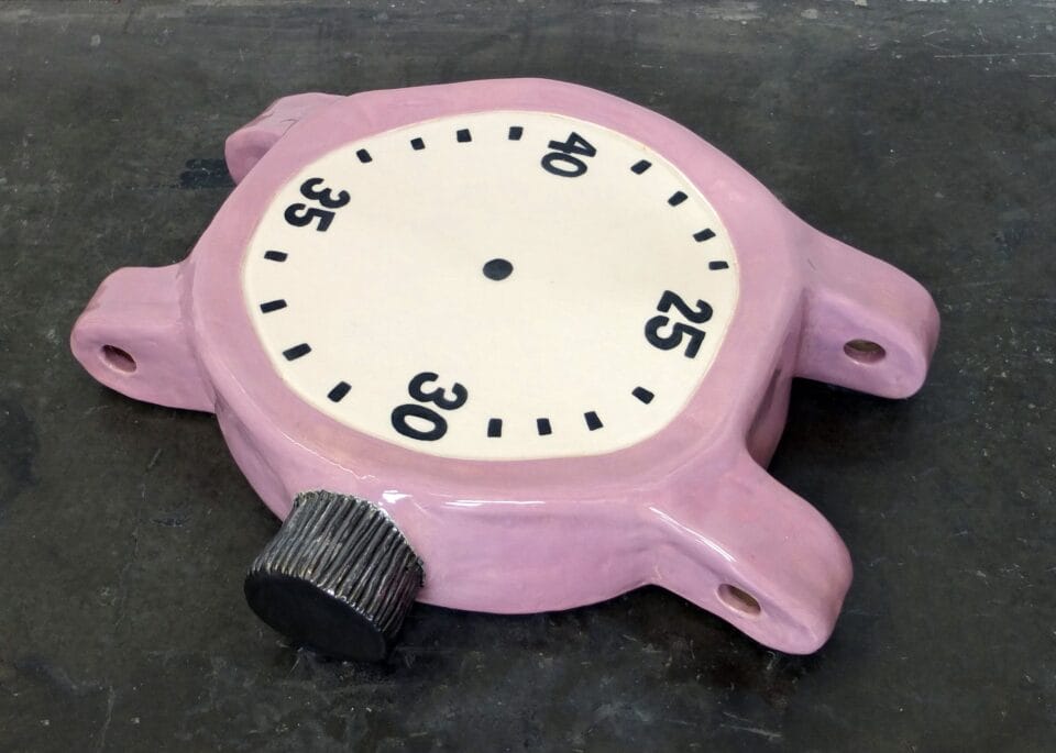 a ceramic sculpture of a clock with pink detail