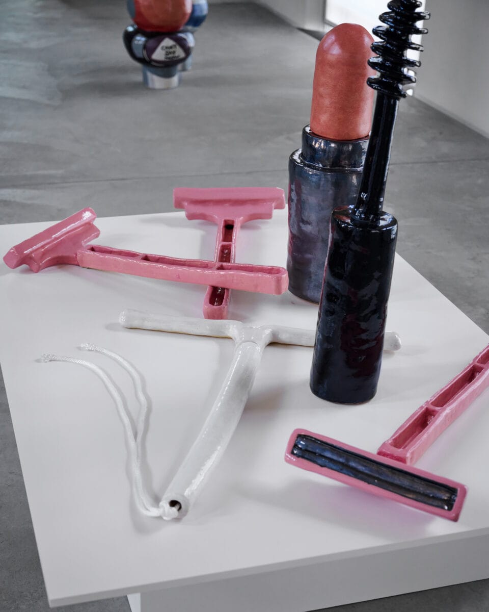 large-scale ceramic sculpture of mascara, lipstick, pink razors, and an IUD