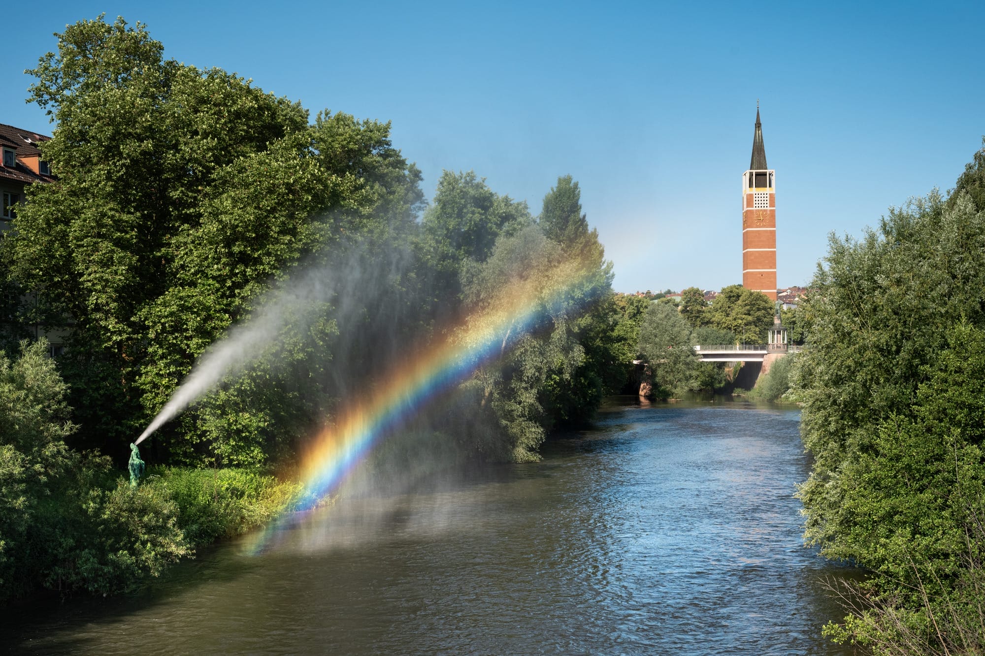 along a river, a fountain sprays water as a rainbow appears to mimic the arch of water it lets off