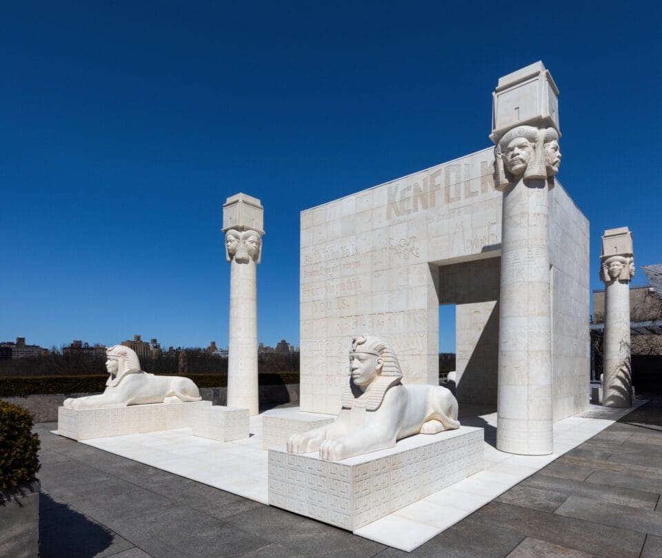 a large outdoor installation mimicking ancient Egyptian palace architecture, with Black figures' faces on the capitals