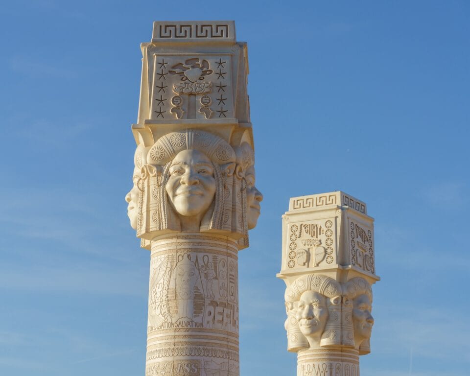 the tops of two columns, part of a large outdoor installation mimicking ancient Egyptian palace architecture, with Black figures' faces on the capitals