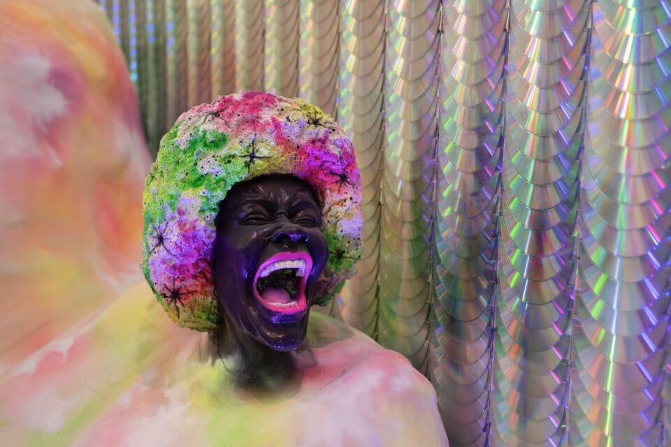 a detail of a large-scale installation showing a Black woman's head with a colorful afro, with her mouth open as if singing or screaming