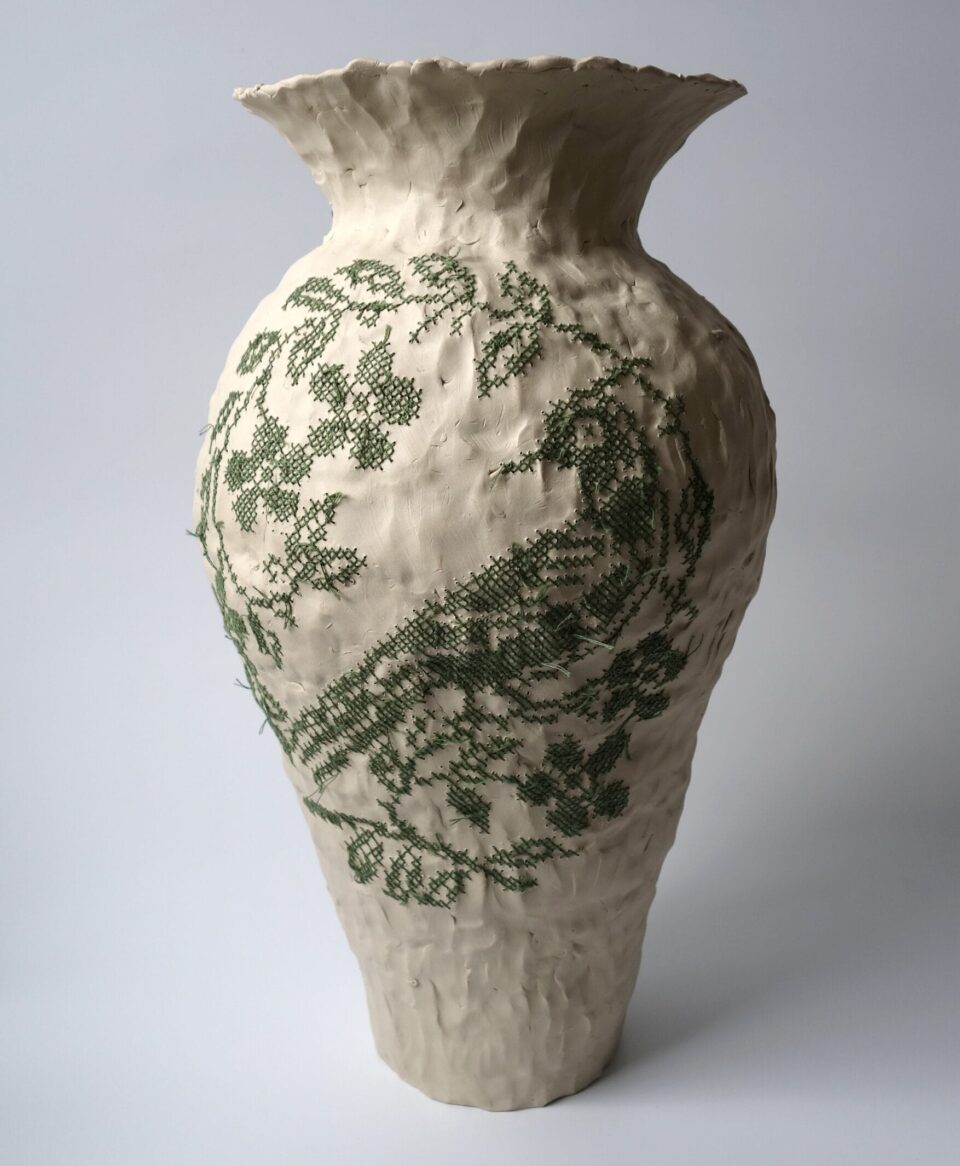 a white porcelain vessel embroidered with green cotton thread