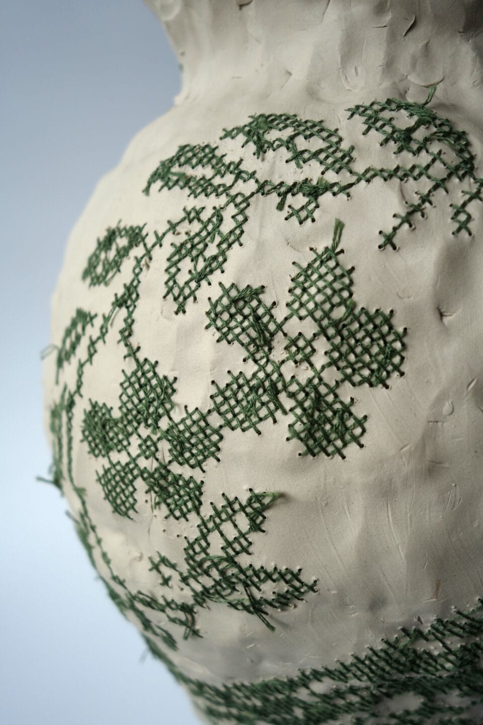 a white porcelain vessel embroidered with green cotton thread