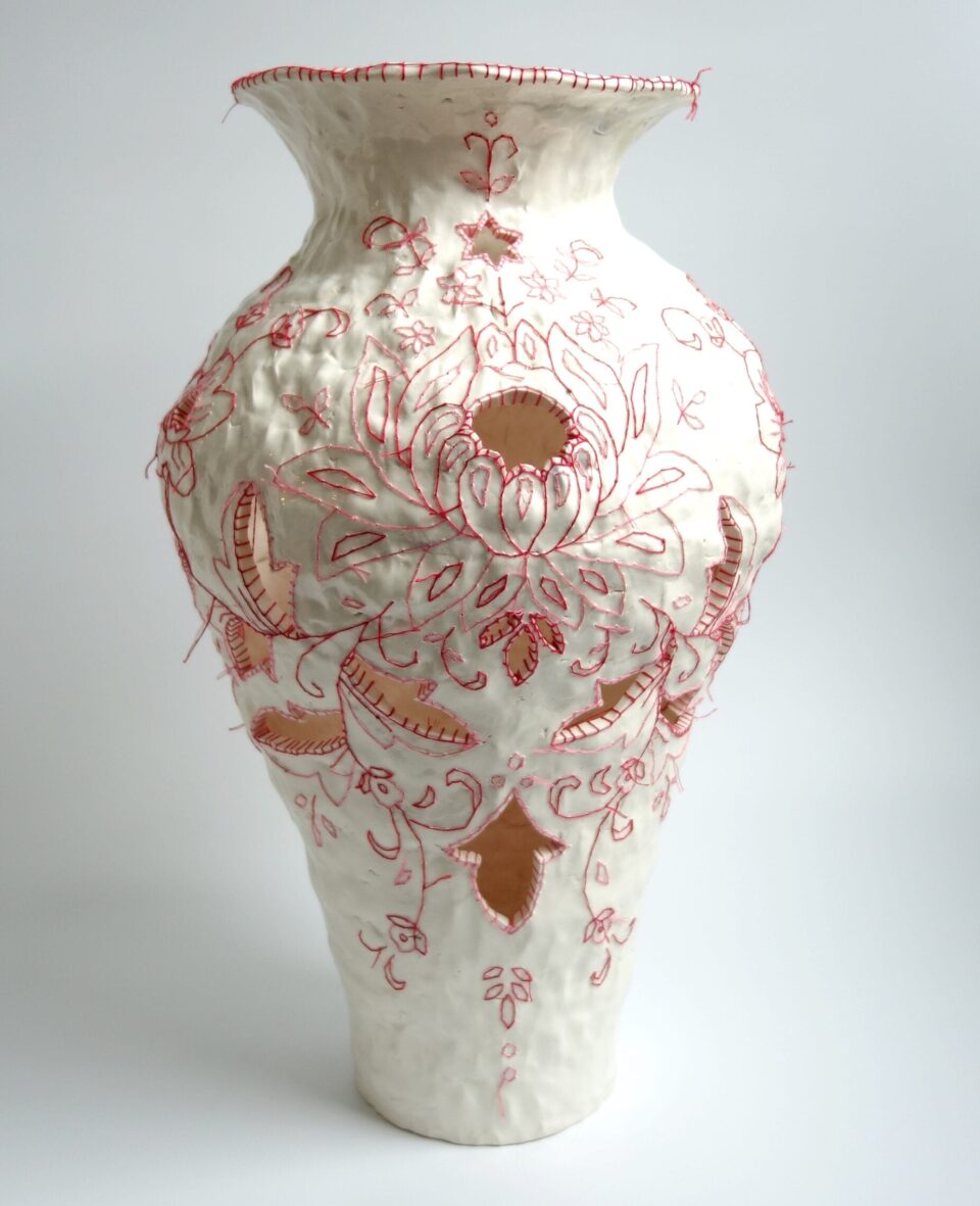 a detail of a white porcelain vessel embroidered with red cotton thread