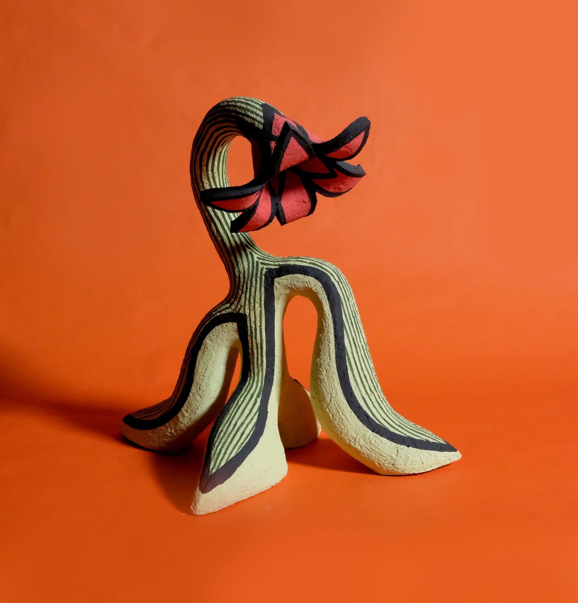 an abstract ceramic sculpture of a flower that stands up on its leaves with a droopy red blossom