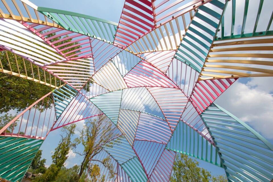 looking up from the interior of a colorful metal outdoor installation shaped like a dome with geometric facets