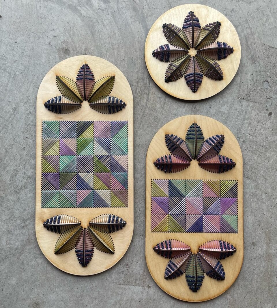 a trio of vibrant embroidered sculptural flowers on wood oval panels. two of the larger works contain a patchwork int he center of two halved flowers, while the smaller is a perfectly round bloom