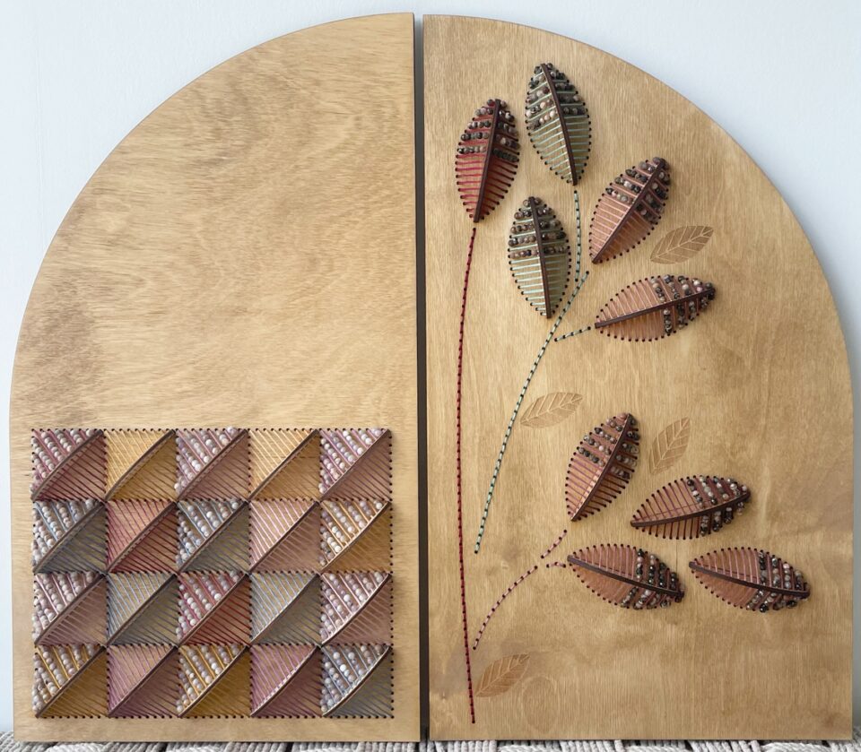 a wooden panel with a curved top edge. an embroidered patchwork is on the left side and sculptural embroidered leaves are on the right