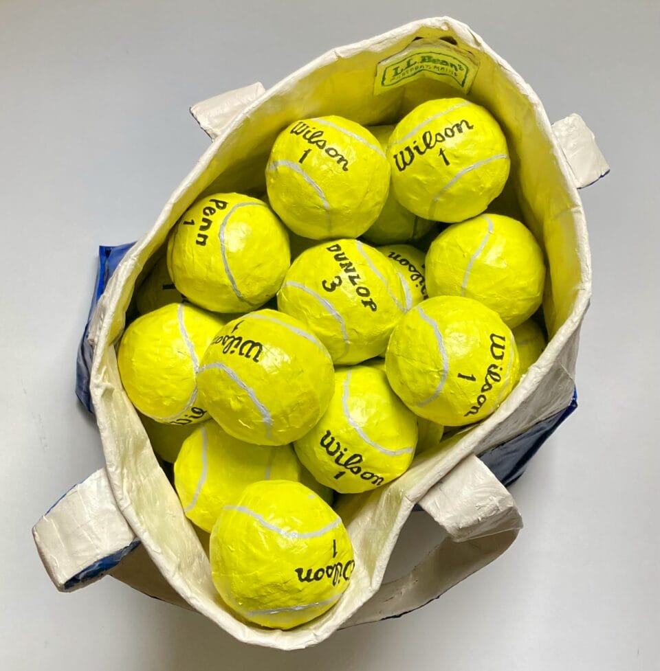 a paper mache sculpture of bright yellow wilson tennis balls in an ll bean canvas tote