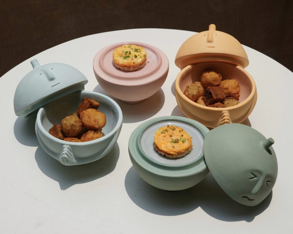 serving bowls shaped like heads in pastel hues hold cooked food inside.