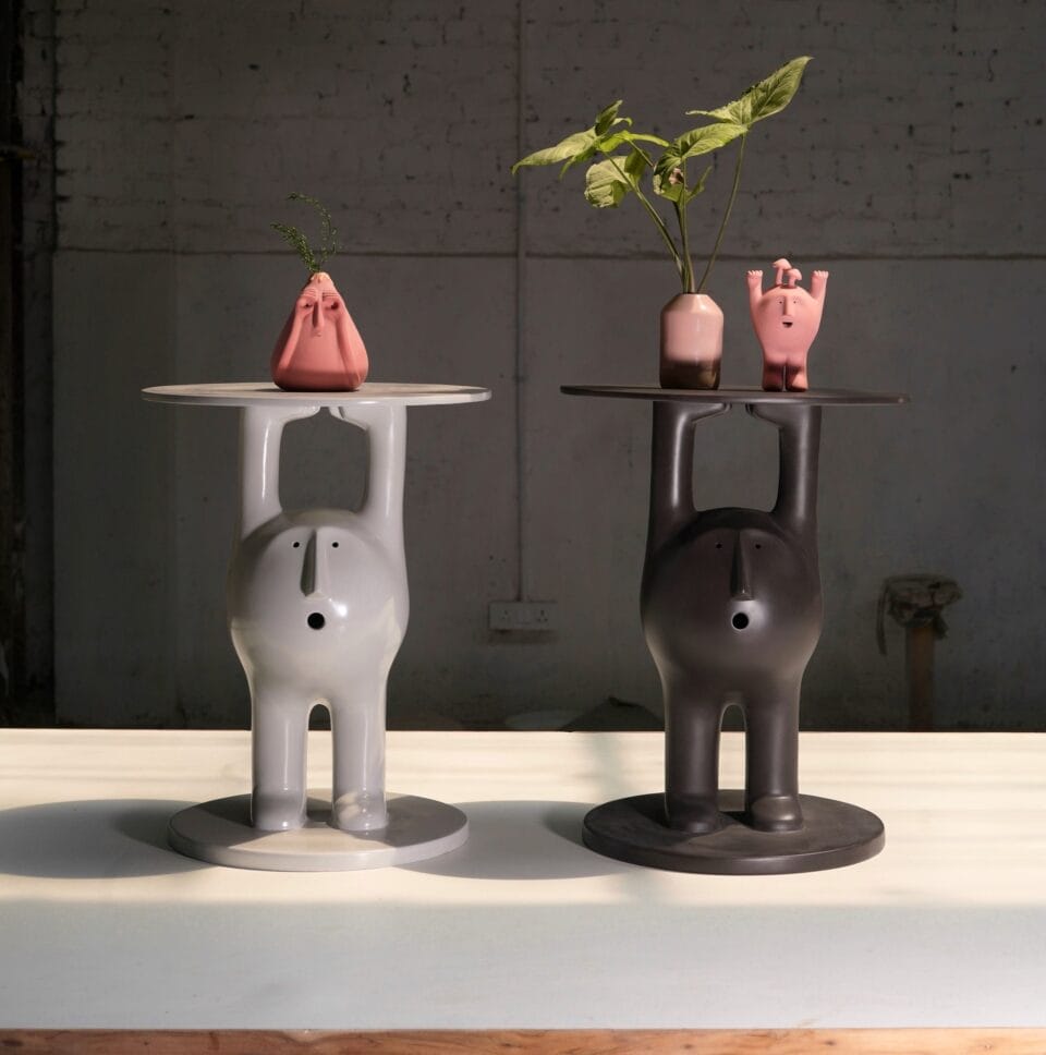 two ceramic figures stand with their arms carrying a functional tray above their heads.