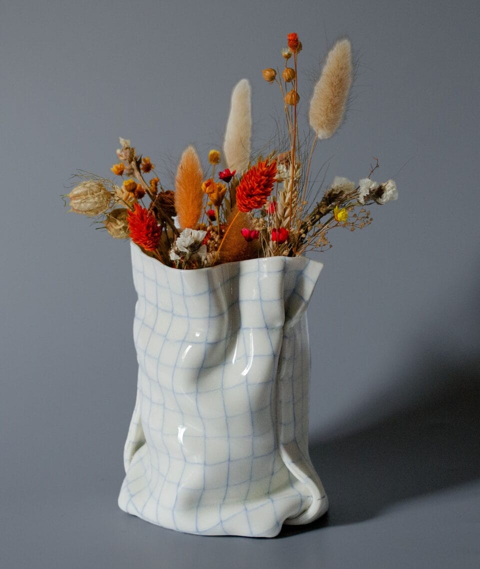 a white ceramic vase that appears to be made of paper holds flowers