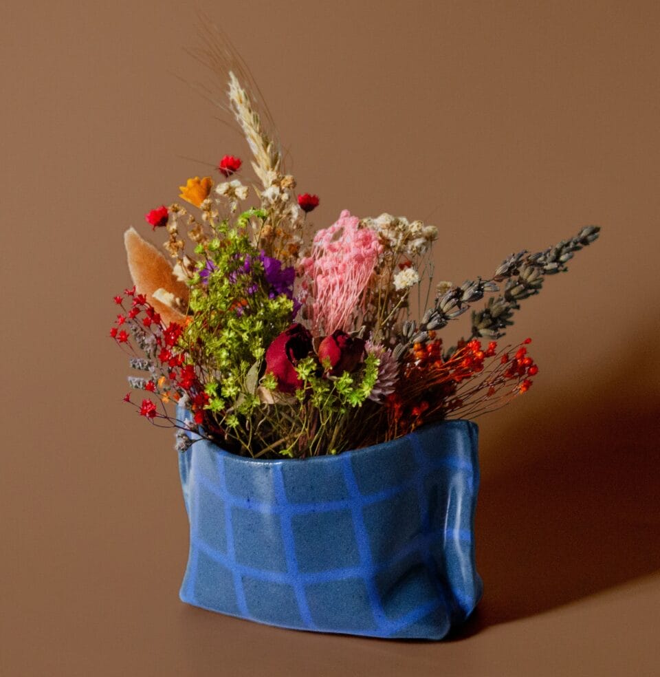 a blue ceramic vase that appears to be made of paper holds flowers