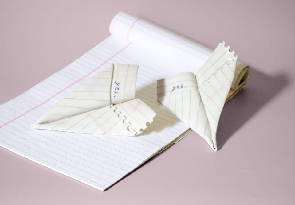 two ceramic paper airplane sculptures atop white notepad 