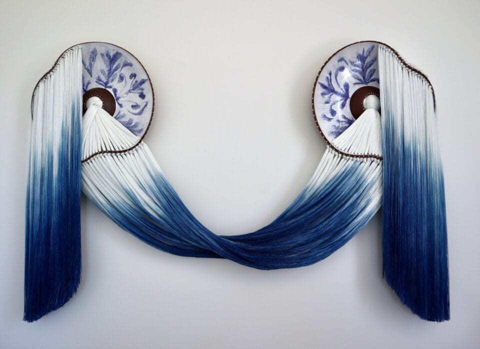 a wall installation made using blue-and-white fiber and blue-and-white glazed ceramic plates with the fiber connecting through holes in the plates and draping elegantly