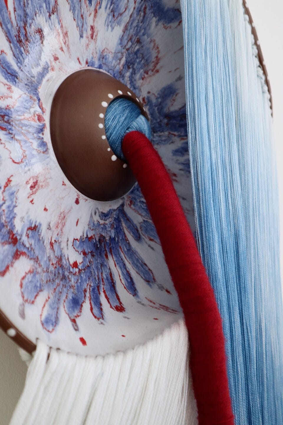 a detail of a wall installation made using blue-and-white and red fiber and blue-and-white glazed ceramic plates with the fiber connecting through a hole in the plate