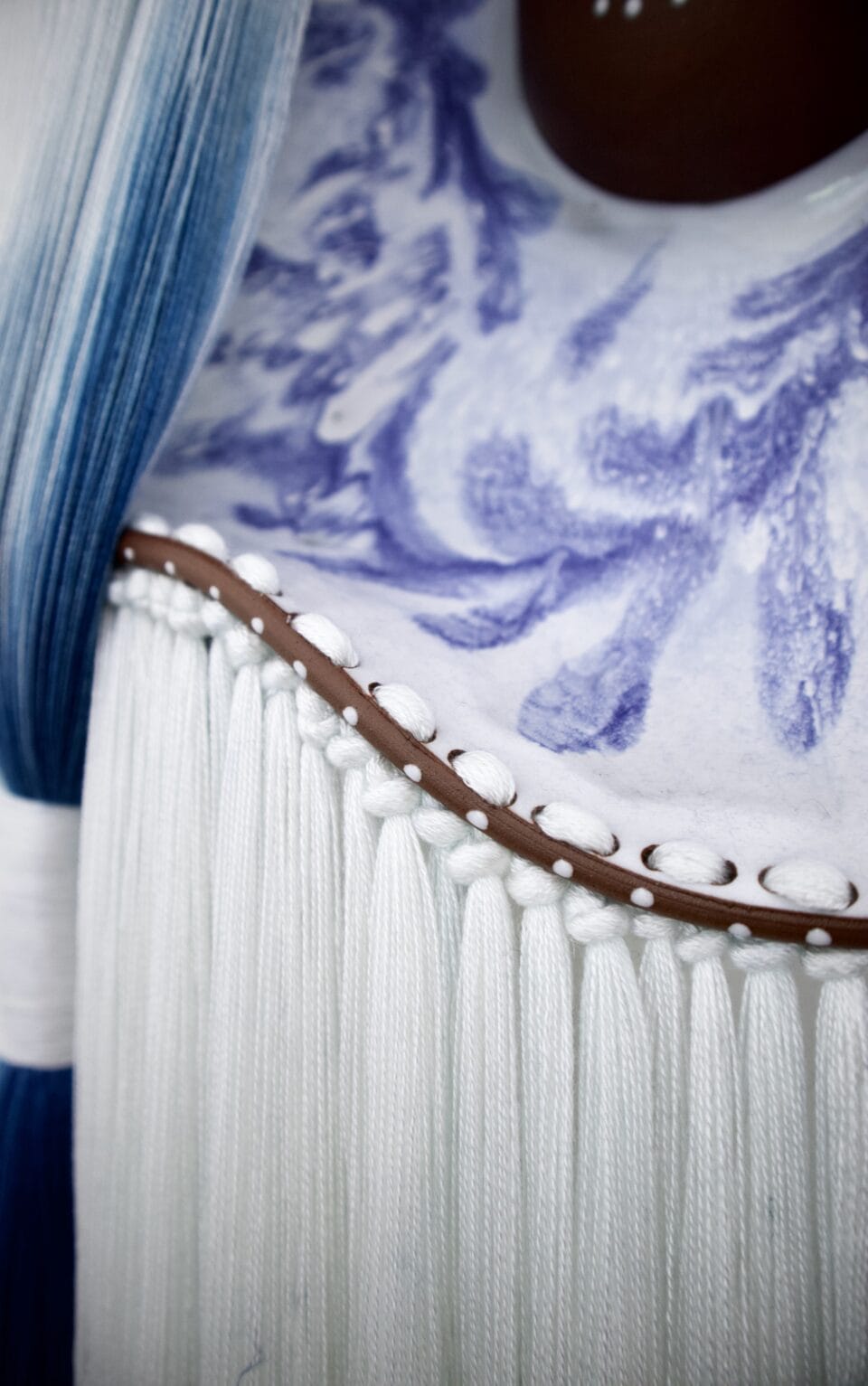 a detail of fiber knotted around the edge of a blue-and-white glazed ceramic plate, part of a larger sculpture