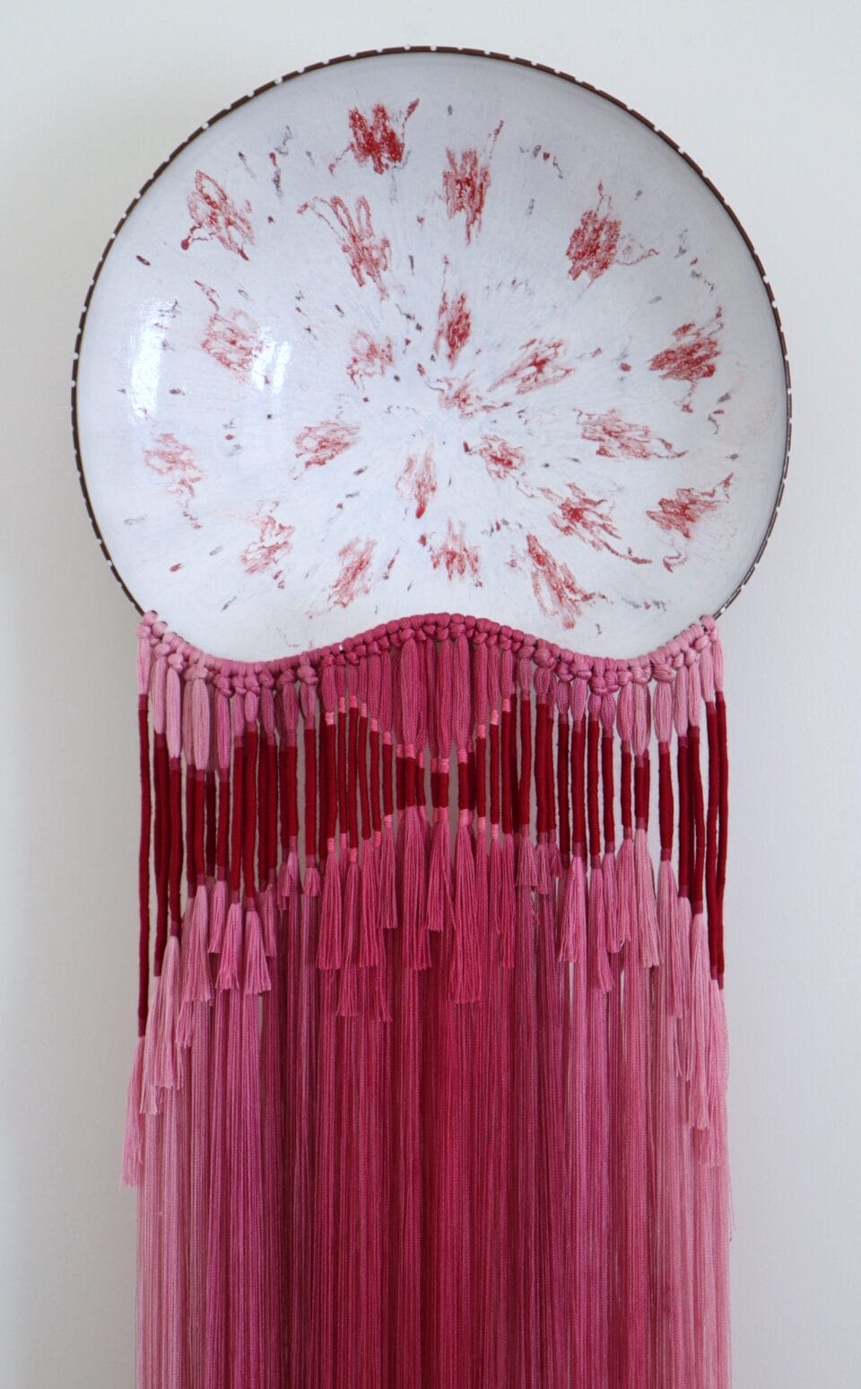 a glazed ceramic plate with red details, with a cascade of red fiber attached to the bottom, installed on a white wall