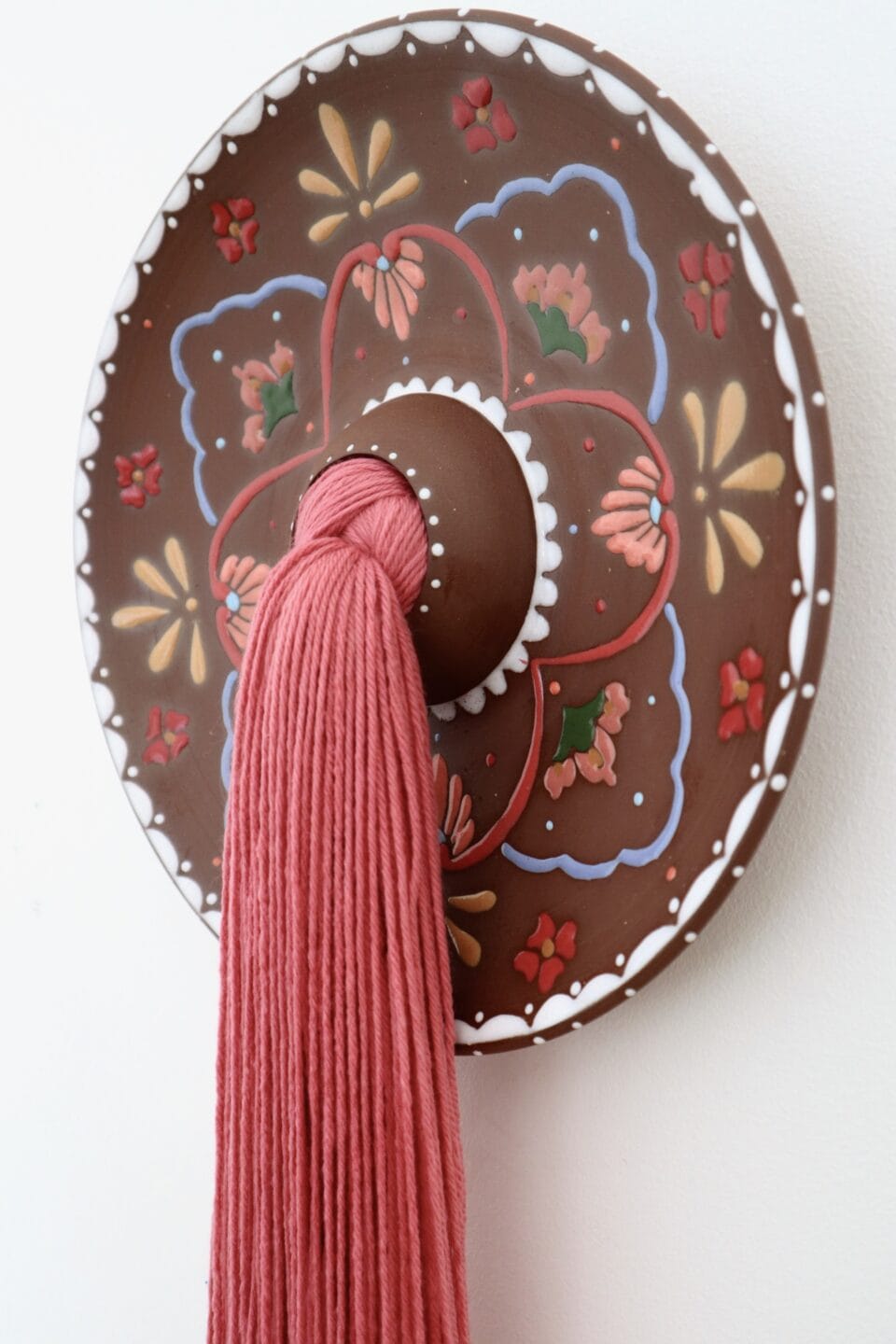 a detail of a large tuft of red fiber emerges from a central hole in a decorated ceramic plate, installed on a white wall