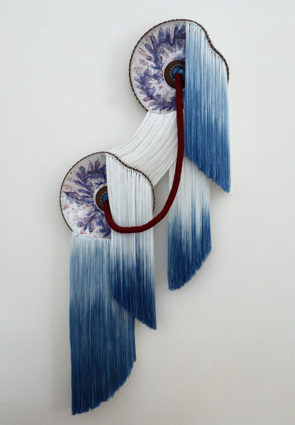 a wall installation made using blue-and-white fiber and blue-and-white glazed ceramic plates with the fiber connecting through holes in the plates and draping elegantly