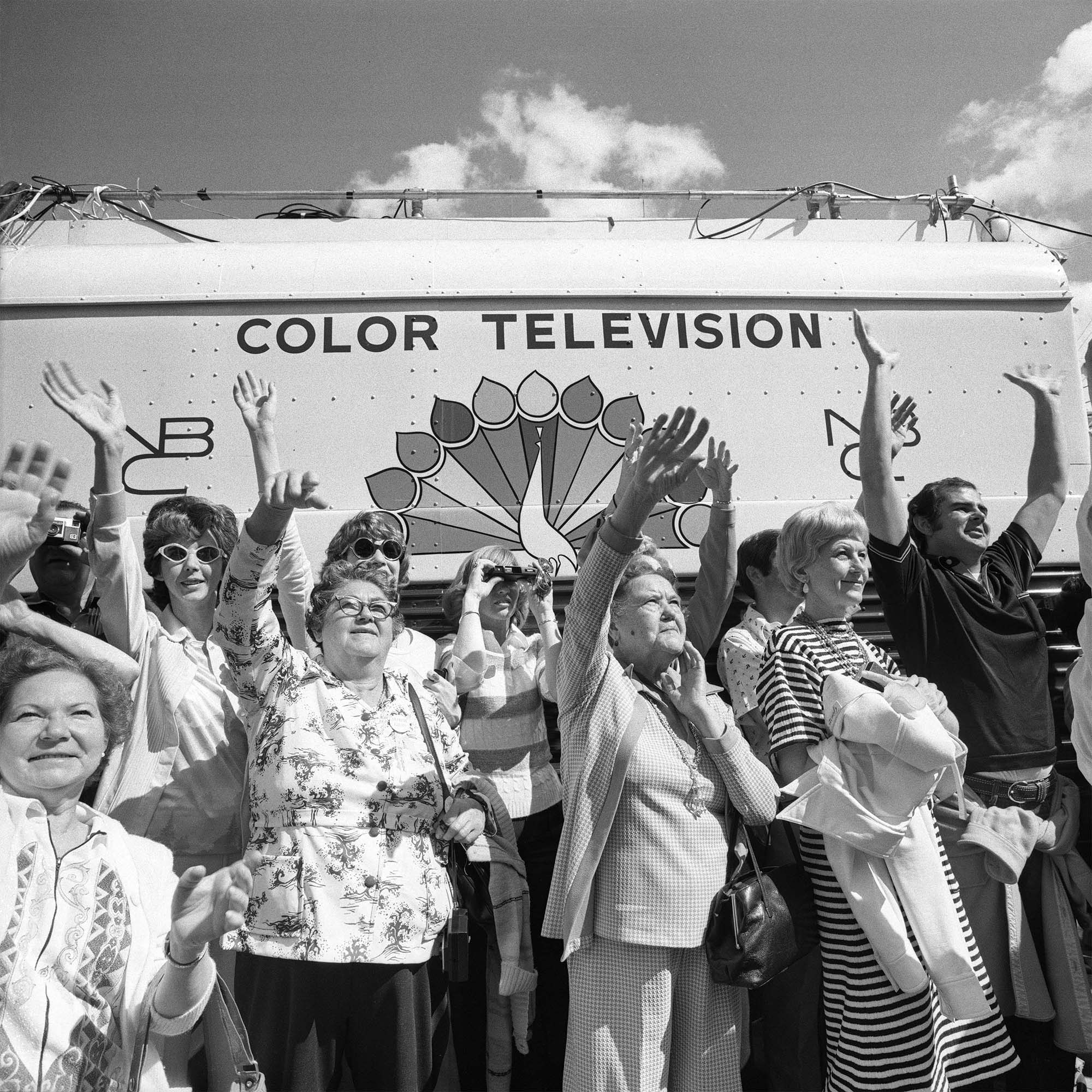 a black and white photograph of a crowd of people watching and waving in front of a vessel that reads "color television"