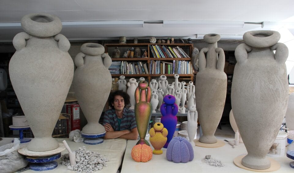 the artist, Maxwell Mustardo, pictured in his studio among large unglazed ceramic vessels