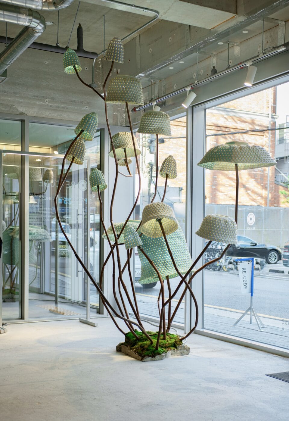 an installation of mushroom-like, abstract lighting fixtures made from woven material, viewed in daylight