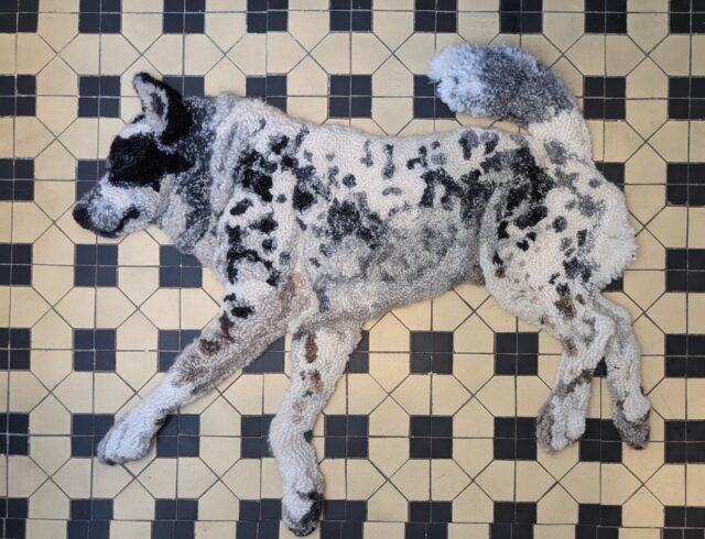 a realistic relief textile work of a dog lounging on a tiled floor, made via rug hooking