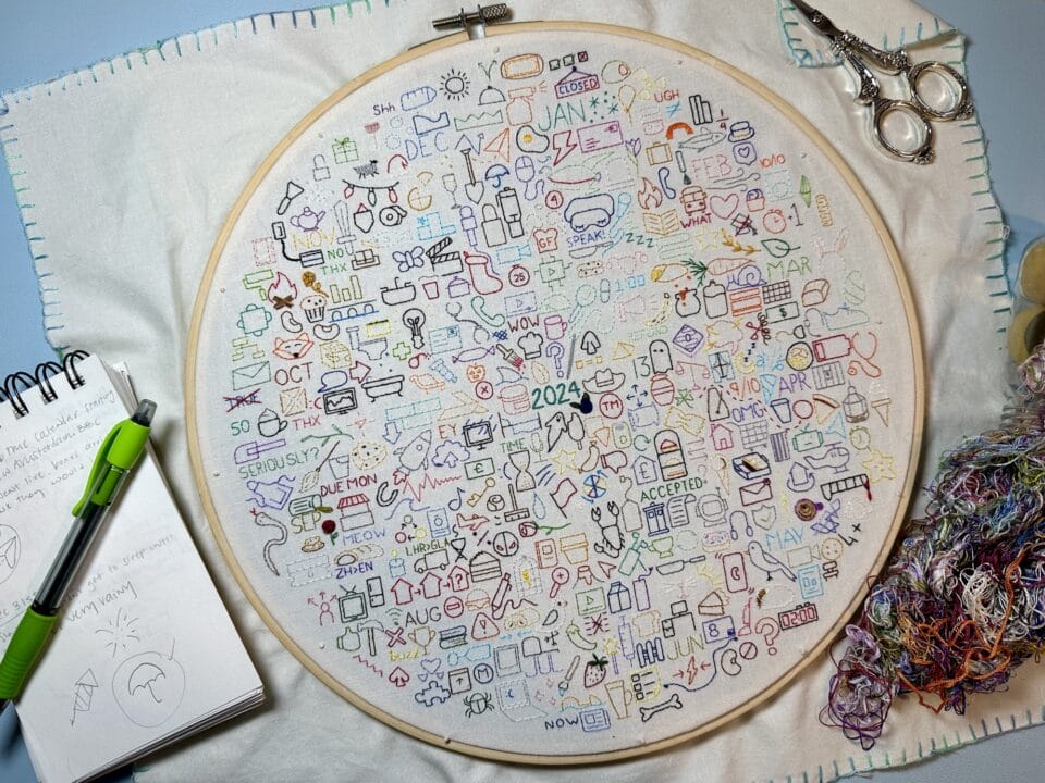 an embroidery hoop with numerous embroidered icons in different colors, each icon representing a day of the year