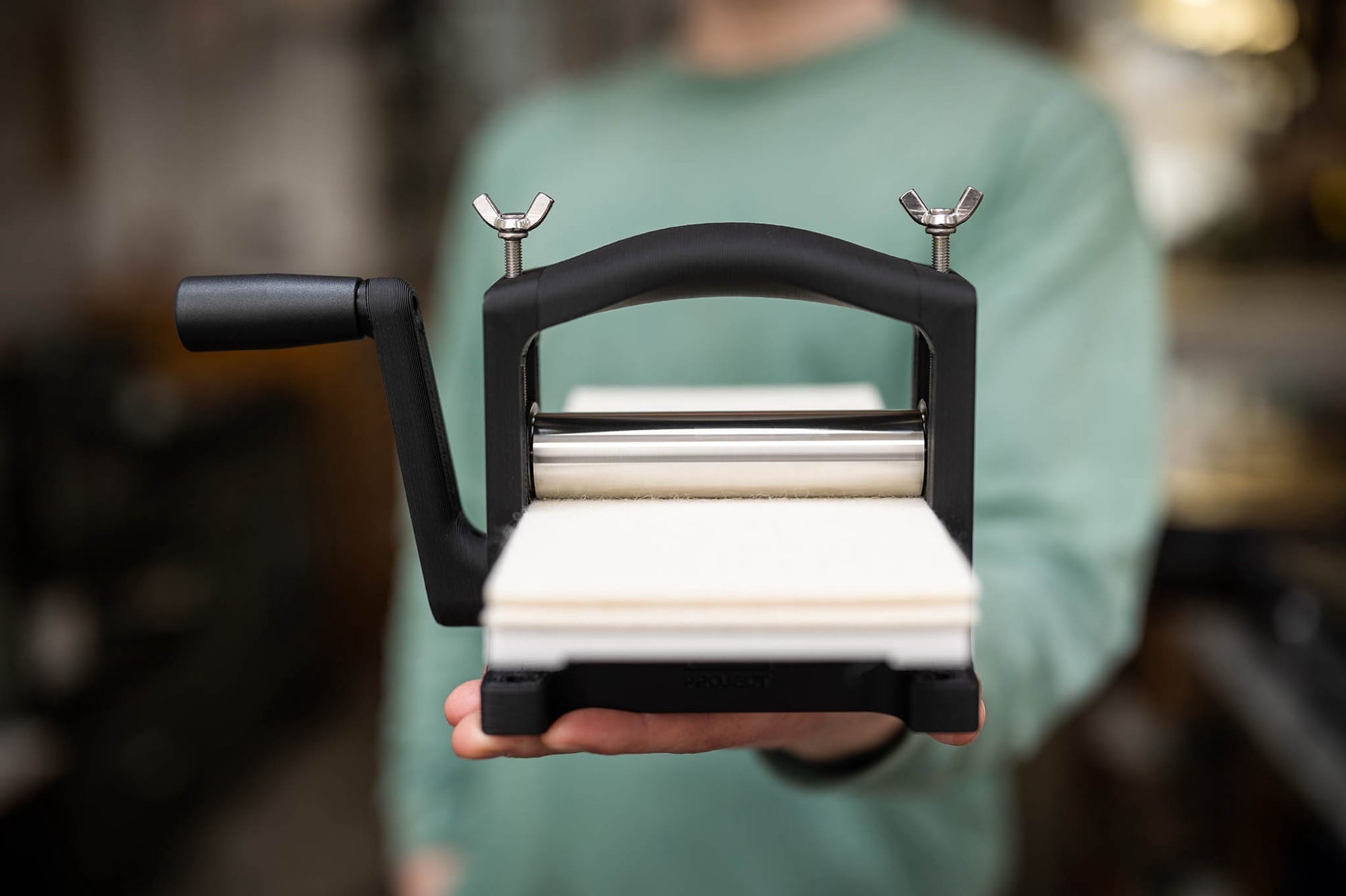 a white hand holds a black printing press with white paper