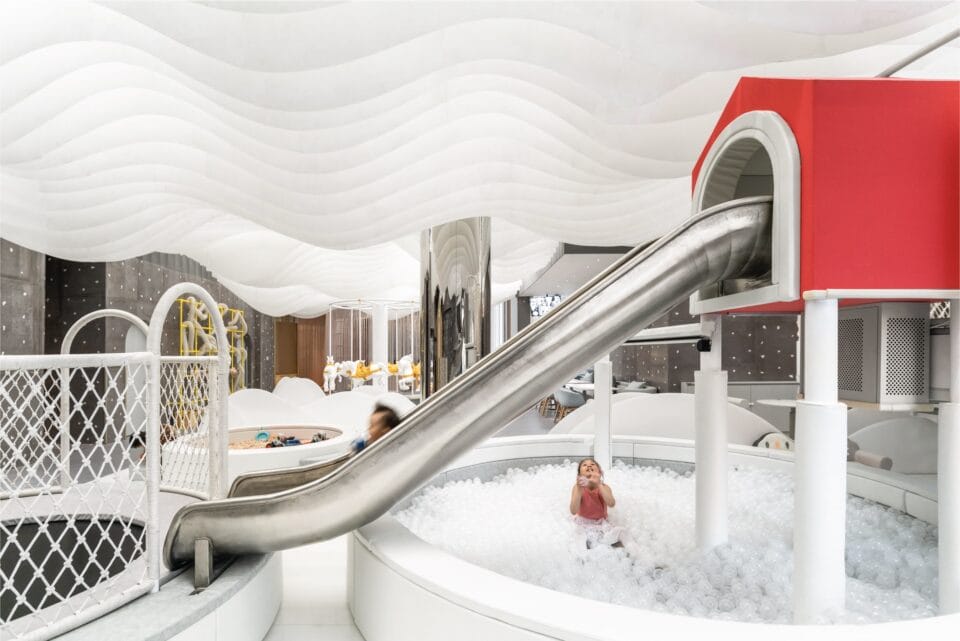 a child plays in a pit of white toys with a silver slide above