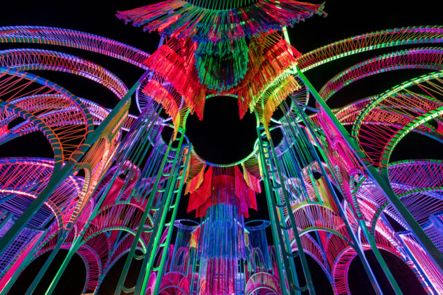 a detail of a vibrantly colored architectural pavilion made of metal poles and rope at night