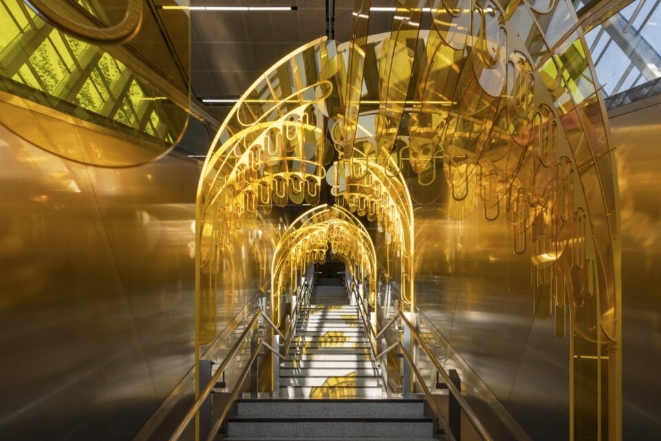 a yellow installation made of undulating pieces of arcylic, placed over a stairwell in a transit station