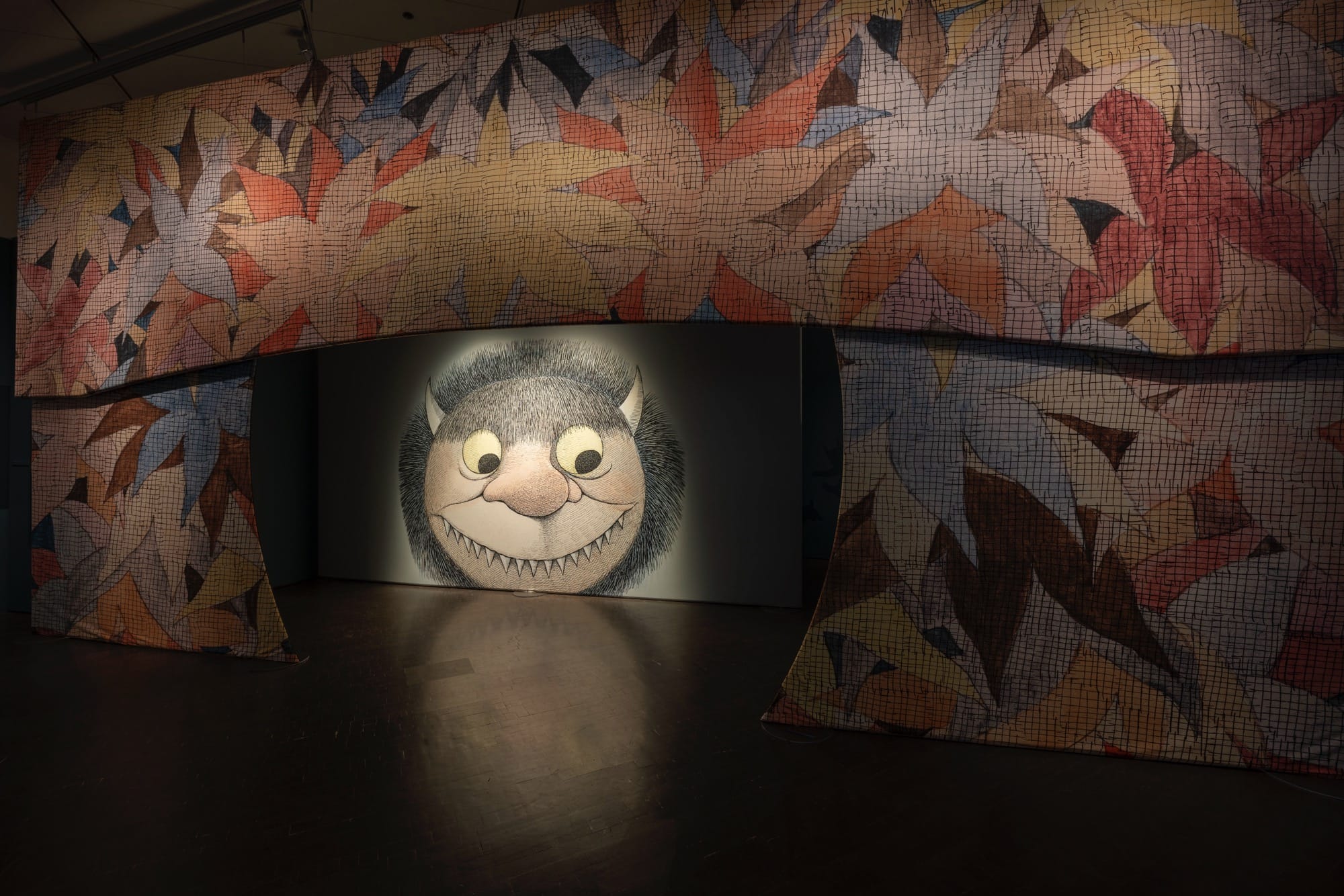 an installation view of the entrance to a Maurice Sendak exhibition in Denver, showing an arched entryway with one of the "wild things" from 'Where the Wild Things Are'