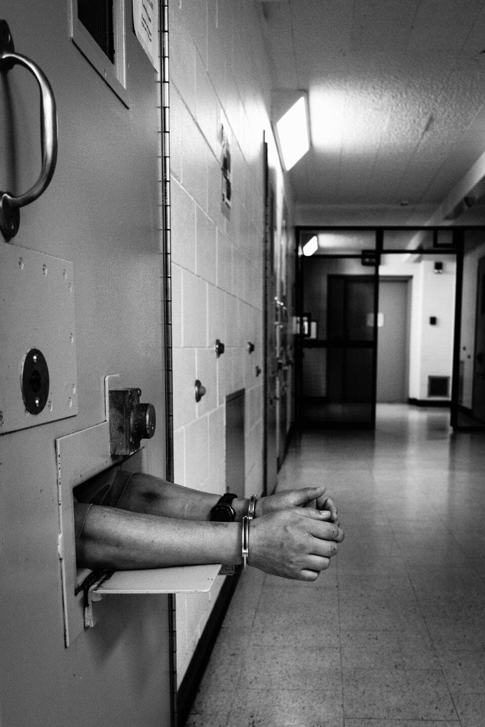 a black and white photo of two handcuffed hadns sticking through a door in a wall 