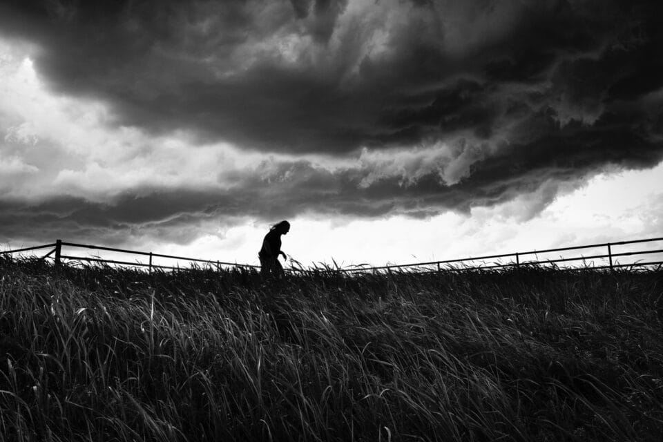 a black and white photo of a person walking along a fence