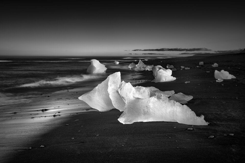 a black-and-white photograph of the shoreline with large ice chunks on the beach in Iceland