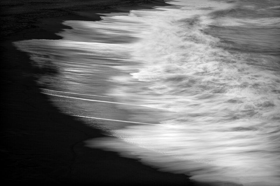 a black-and-white photograph of surf on a black beach in Iceland