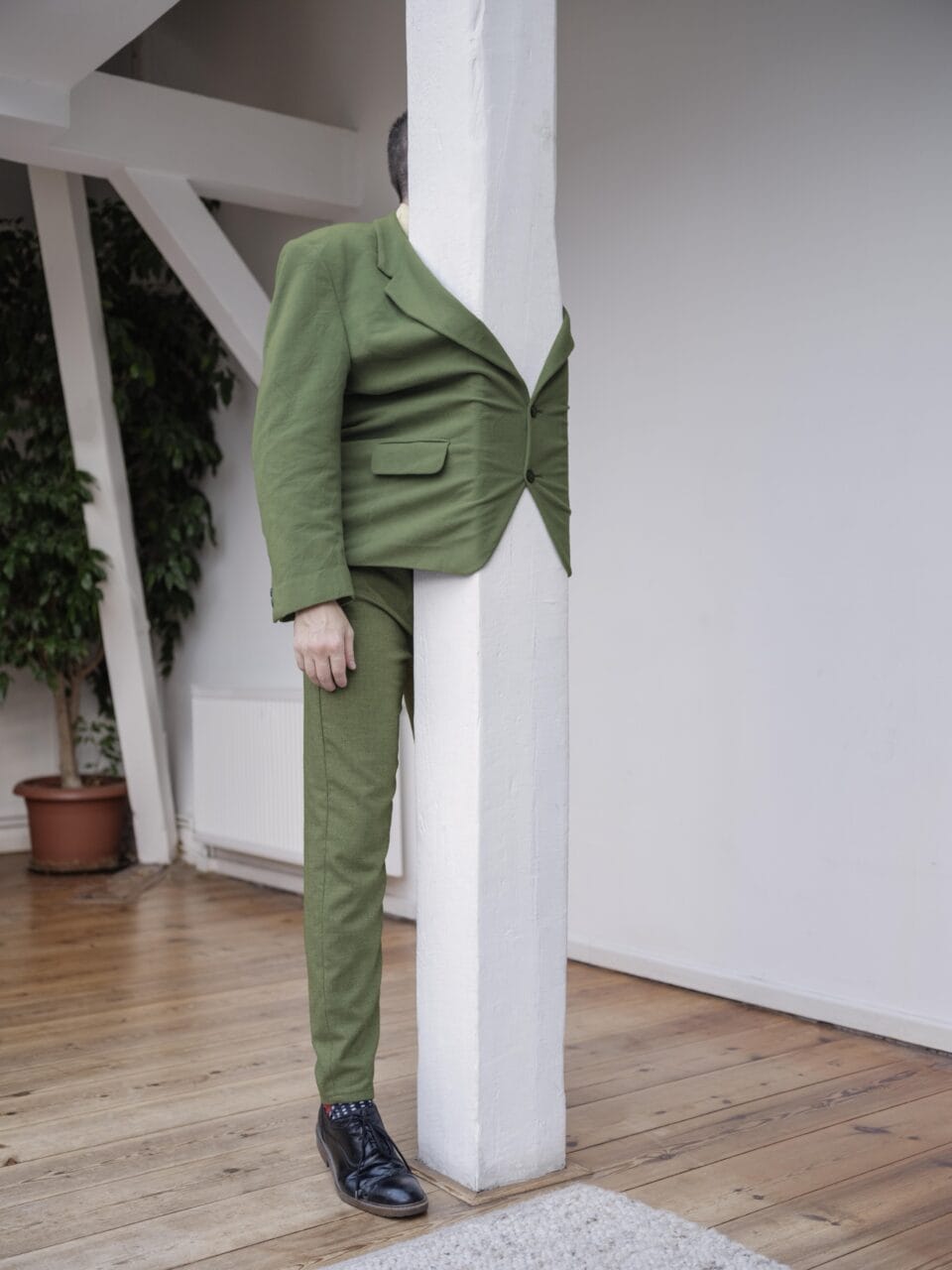 a man in a green suit has his jacket buttoned around a white post