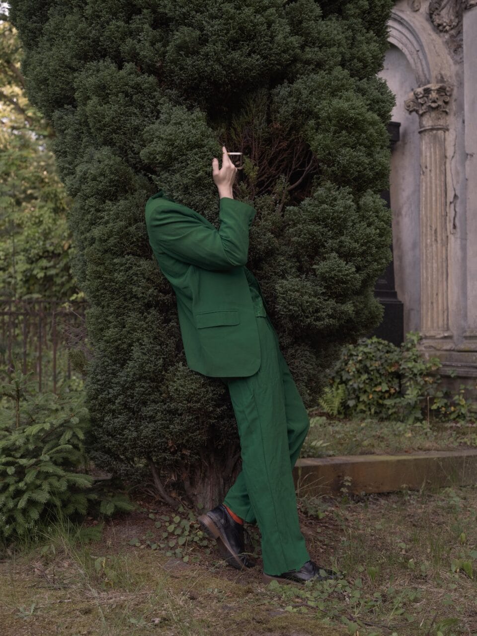 a man in a green suit is smoking while his head is in a bush